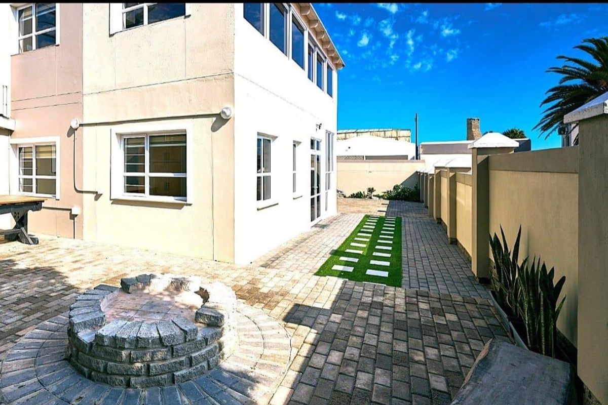 A well-maintained rear exterior area featuring a paved patio, a stone fire pit, and a boundary wall, providing a functional outdoor space.