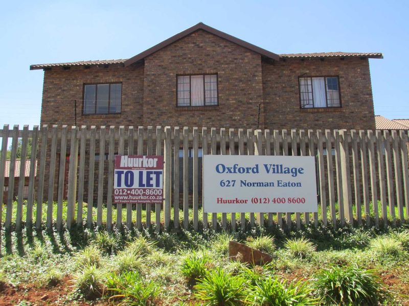 Front elevation of a face-brick apartment complex featuring a concrete palisade fence and secure perimeter electric fencing.