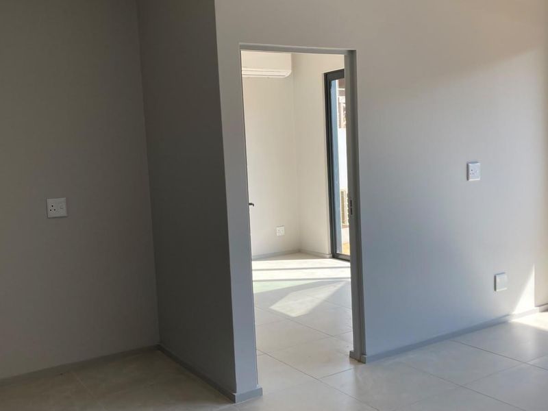 A bright, modern, and empty living area featuring neutral tiled flooring, clean walls, and a sliding glass door leading to an outdoor space.