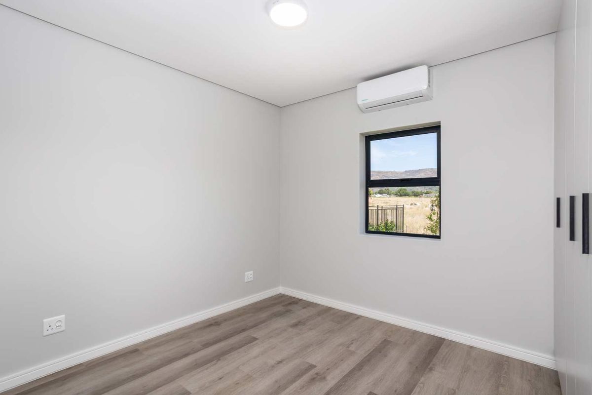 A clean, modern bedroom featuring neutral walls, durable laminate flooring, a built-in wardrobe, and a wall-mounted air conditioning unit.