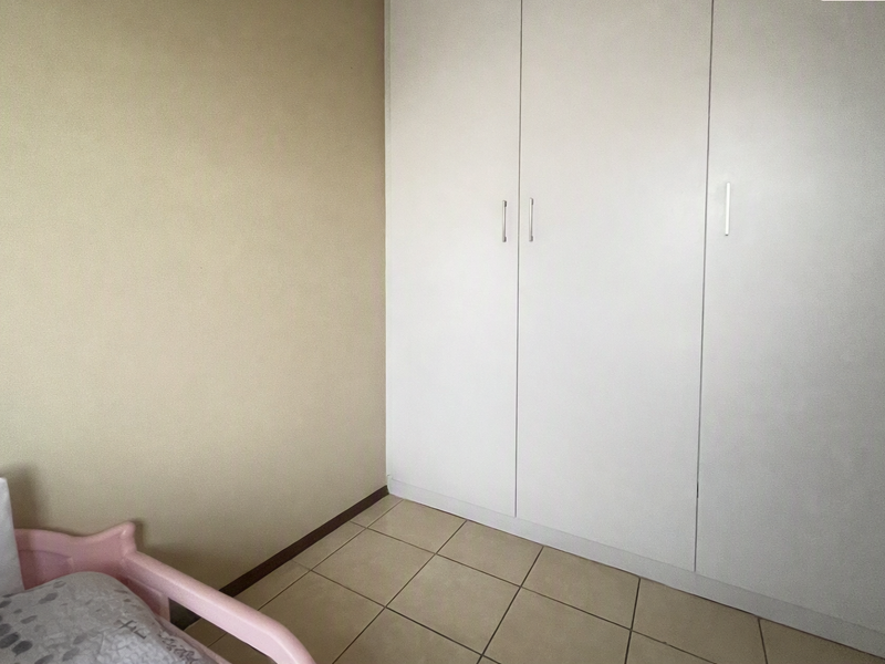 A bedroom featuring neutral wall tones, tiled flooring, and a large white built-in wardrobe providing ample storage space.