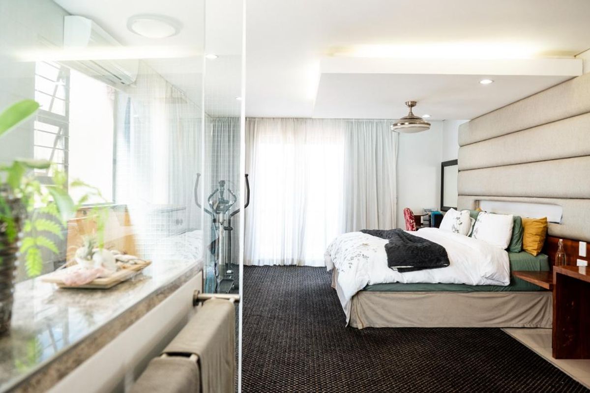 Spacious bedroom featuring a large upholstered headboard, recessed ceiling lighting, and an integrated glass-enclosed bathroom area with modern finishes.