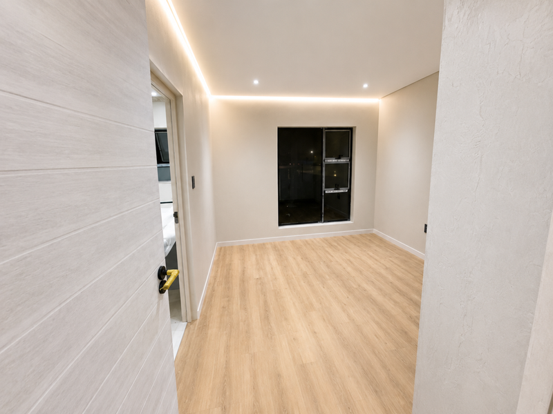 A bright, modern bedroom featuring light wood-look laminate flooring, recessed perimeter LED lighting, and clean neutral finishes.