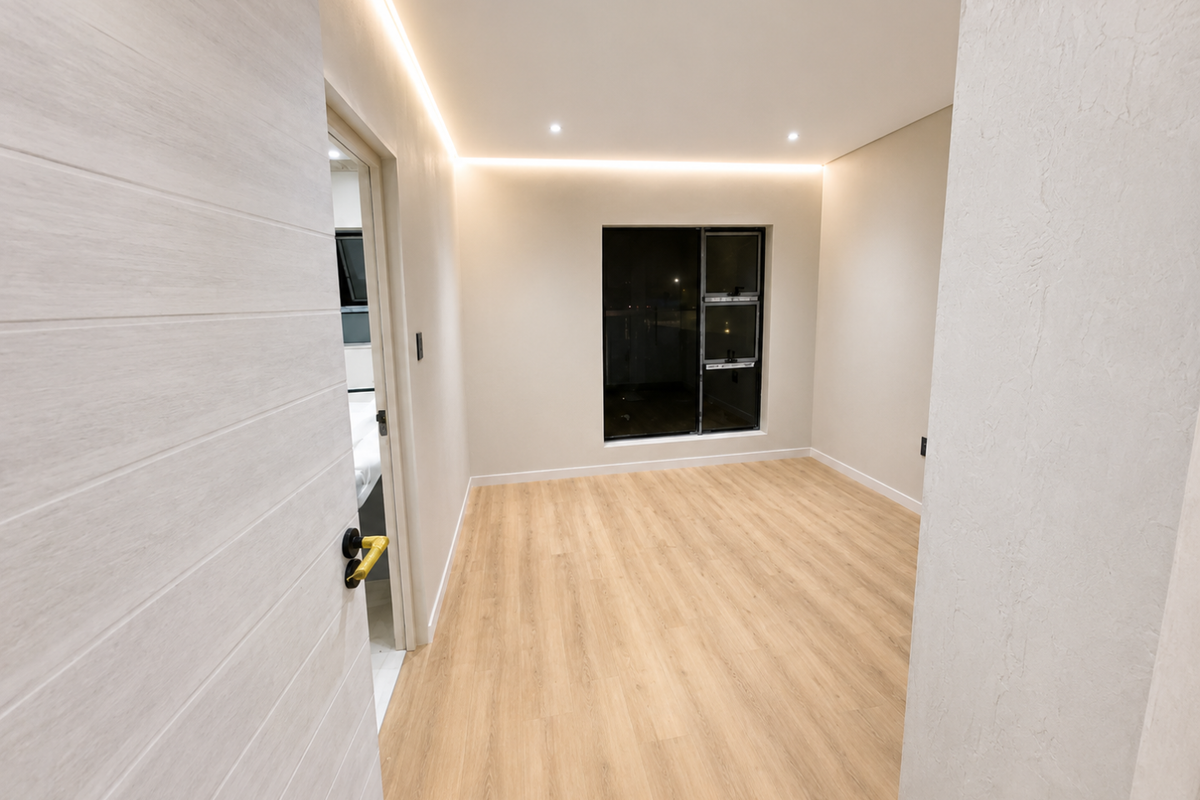 A bright, modern bedroom featuring light wood-look laminate flooring, recessed perimeter LED lighting, and clean neutral finishes.