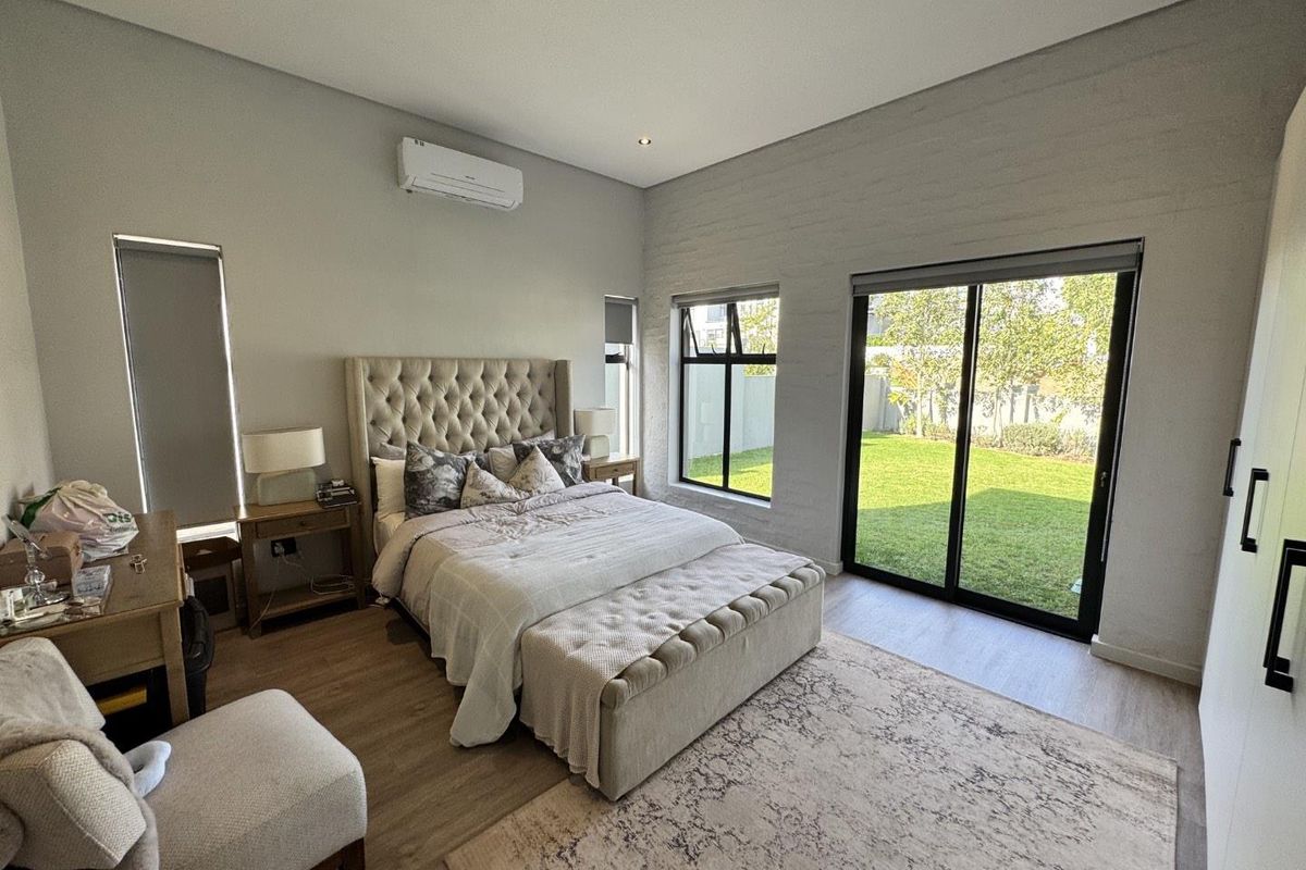 Spacious bedroom featuring modern laminate flooring, recessed lighting, wall-mounted air conditioning, and large sliding glass doors providing direct access to the garden.