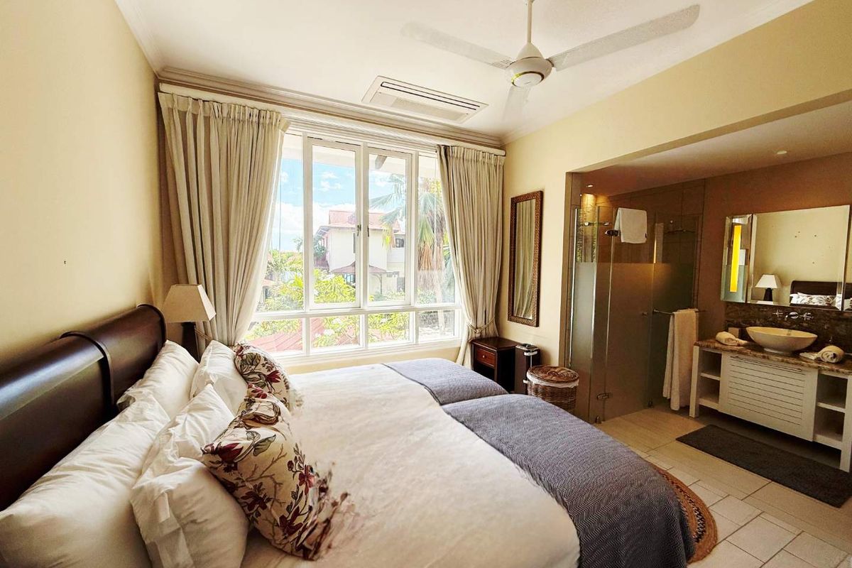 A well-appointed bedroom featuring an en-suite bathroom with a vanity, large window with natural light, and a ceiling fan.