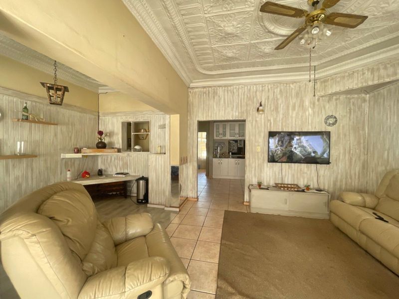 Open plan living area featuring a decorative pressed metal ceiling, ceiling fan, tiled flooring, and timber wall paneling with a pass-through to the kitchen.