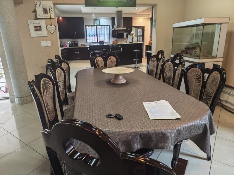 Open plan dining area flowing into a modern kitchen featuring dark cabinetry, a central island, and tiled flooring throughout.