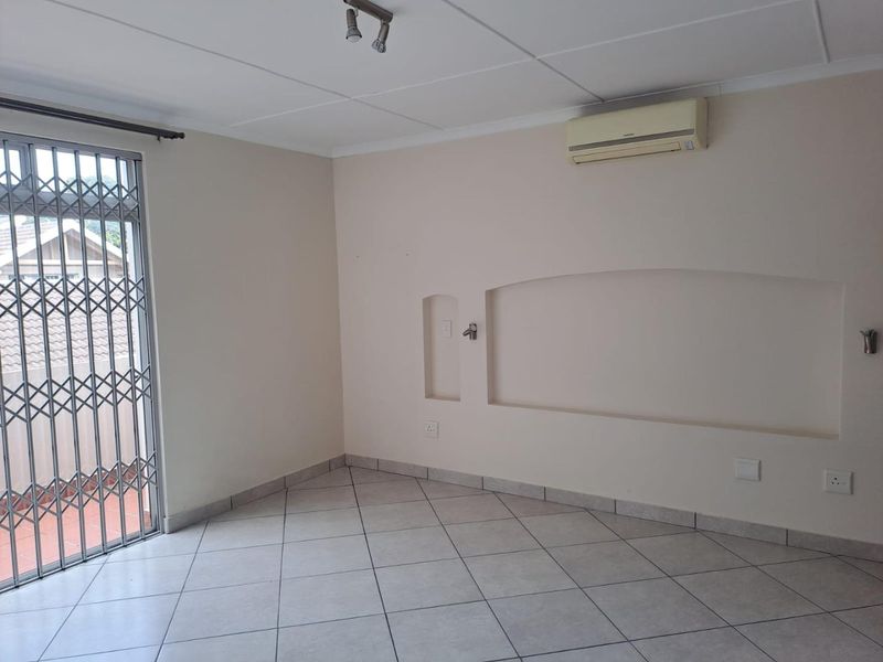 An empty living area featuring tiled flooring, a wall-mounted air conditioning unit, and a decorative recessed wall niche with access to an outdoor balcony.