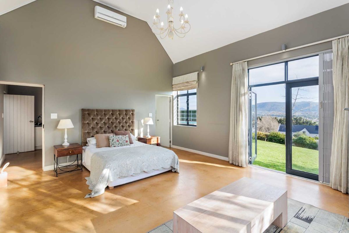Spacious bedroom featuring vaulted ceilings, polished concrete floors, and large glass doors opening to a scenic garden view.