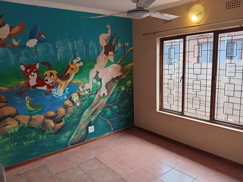 An empty bedroom featuring tiled flooring, a ceiling fan, and a large decorative wall mural, equipped with security bars on the window.