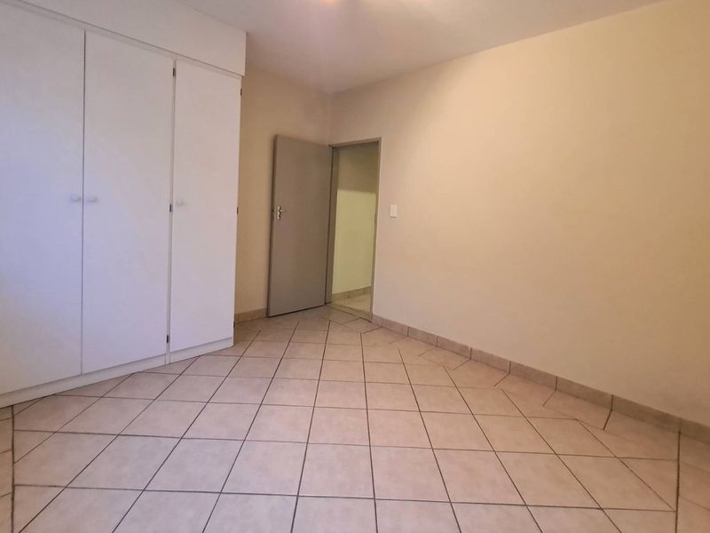 An empty bedroom featuring neutral tiled flooring and built-in cupboards, offering a clean and versatile space ready for personalization.