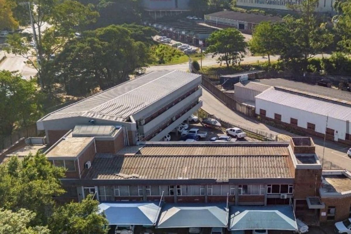 Aerial view of a multi-story commercial property featuring a metal roof, brick exterior, and dedicated covered parking bays.