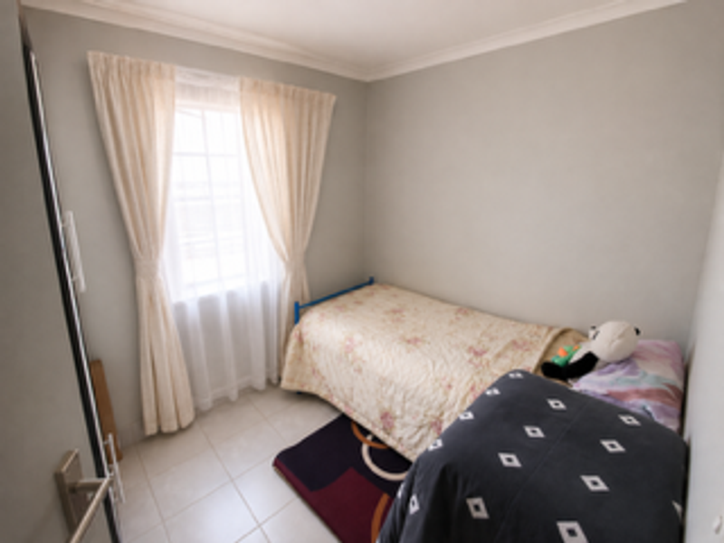 A compact bedroom featuring tiled flooring, neutral wall finishes, and a window with fitted curtains.