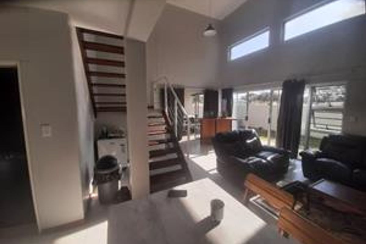 Spacious open-plan living area featuring a staircase, high ceilings with clerestory windows, and large sliding glass doors providing access to the exterior.