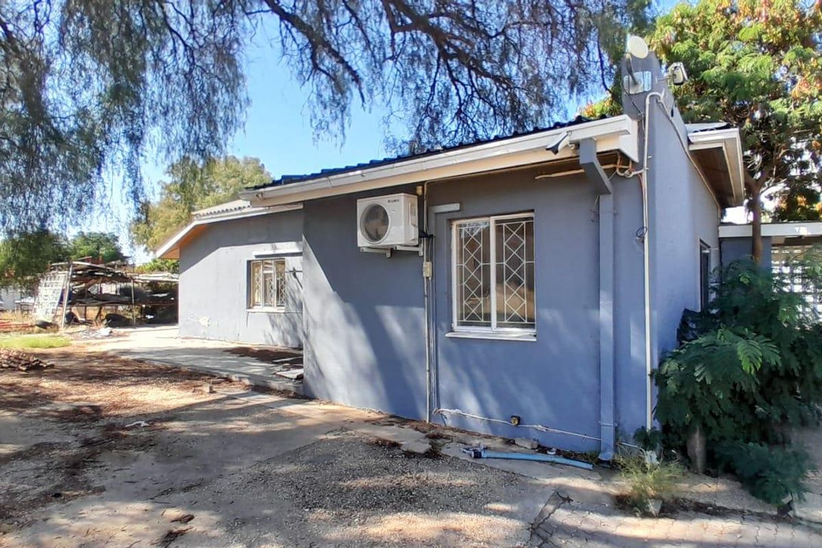 Rear exterior view of the property featuring a painted facade, security-barred windows, and an external air conditioning unit.