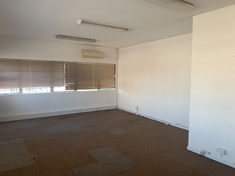 An empty office space featuring carpet tiles, fluorescent lighting, and a wall-mounted air conditioning unit, suitable for a professional workspace.