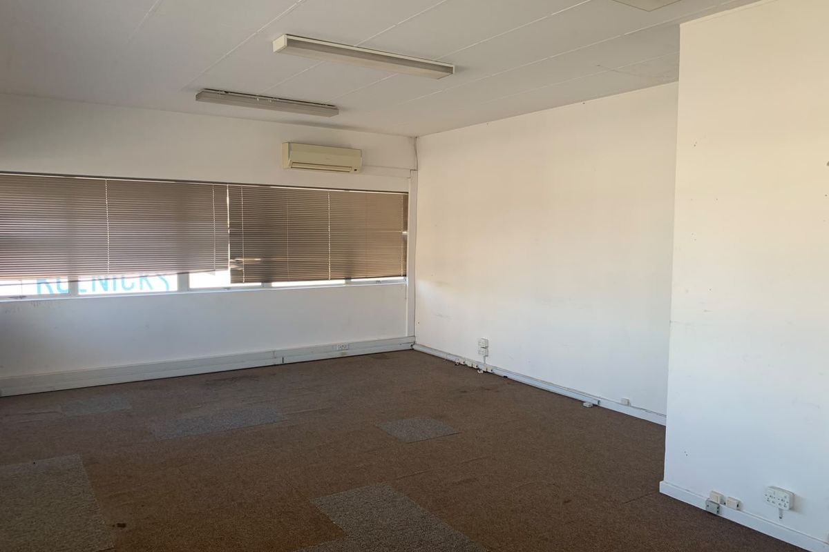 An empty office space featuring carpet tiles, fluorescent lighting, and a wall-mounted air conditioning unit, suitable for a professional workspace.