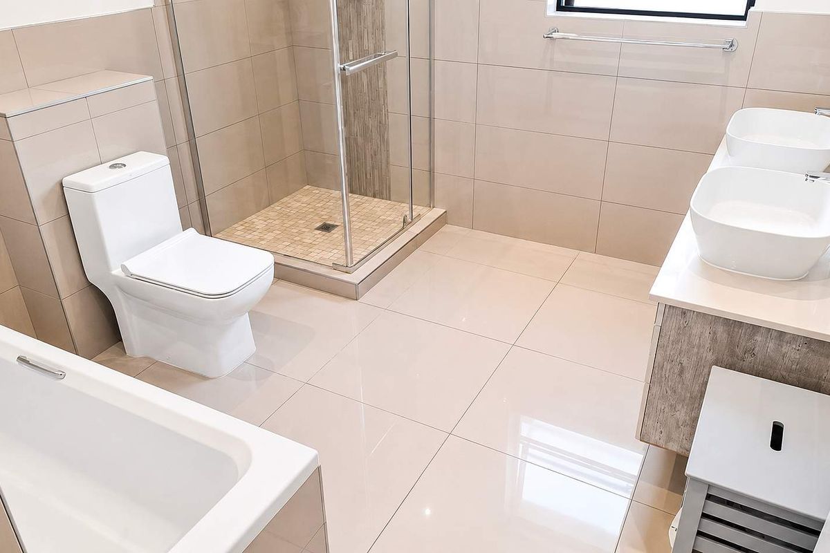 Modern bathroom featuring a double vanity, glass-enclosed shower, and a built-in bathtub with neutral floor-to-ceiling tiling.