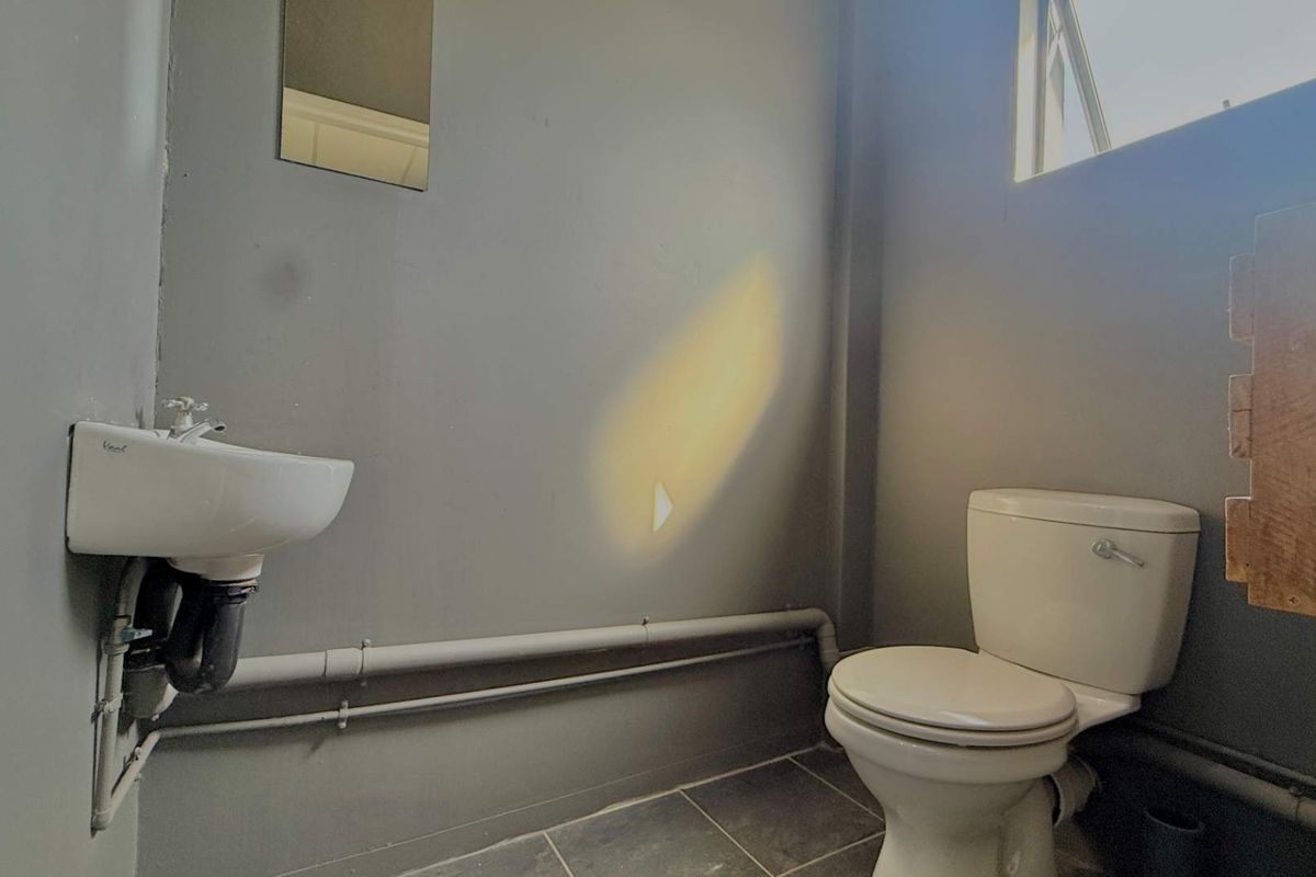 A compact bathroom featuring a wall-mounted basin, toilet, and tiled flooring with exposed plumbing and basic finishes.