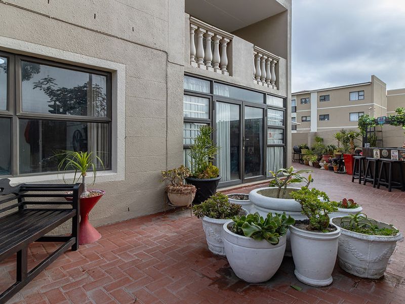 A paved outdoor patio area featuring a balustrade balcony above and direct access to the interior through sliding glass doors.
