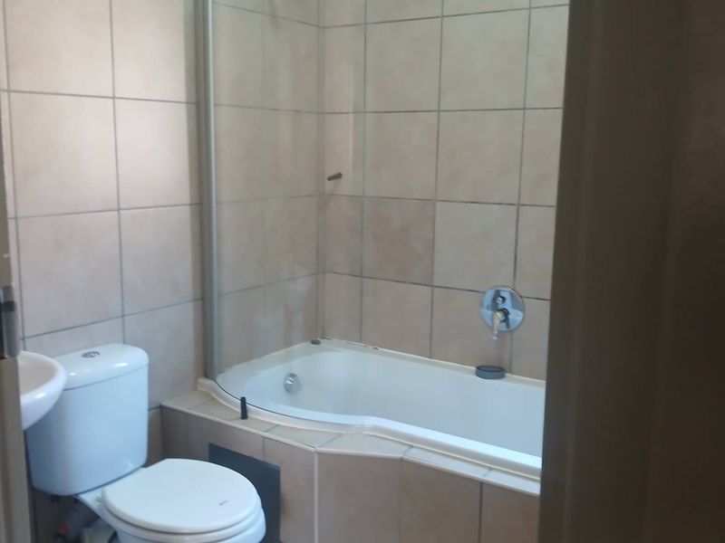 A functional bathroom featuring a bathtub with a glass shower screen, wall tiling, a toilet, and a basin.
