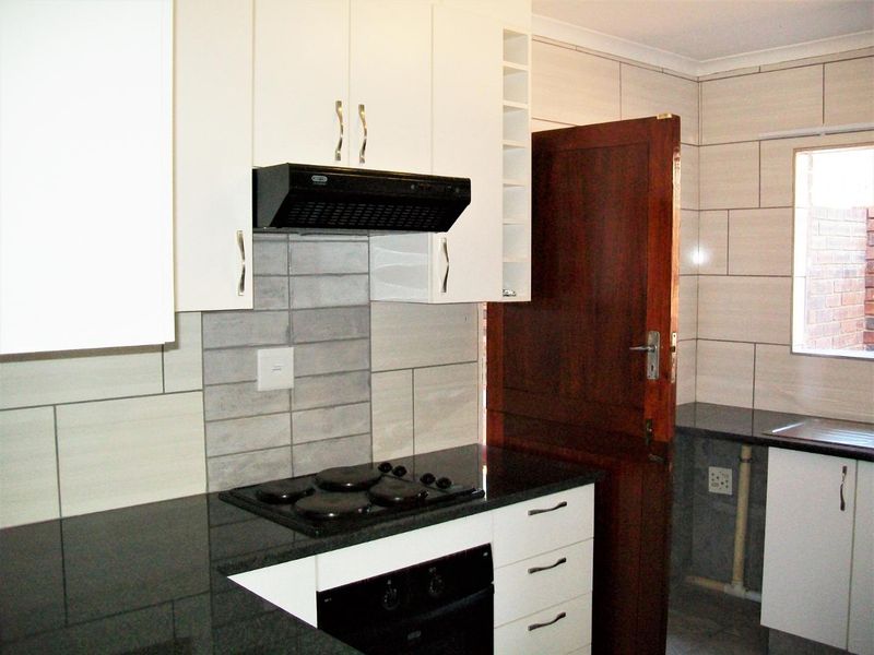 A clean, modern kitchen featuring white cabinetry, dark granite countertops, a built-in oven, and an electric hob with an extractor fan.