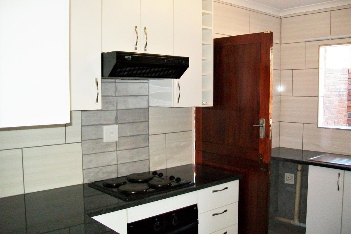 A clean, modern kitchen featuring white cabinetry, dark granite countertops, a built-in oven, and an electric hob with an extractor fan.
