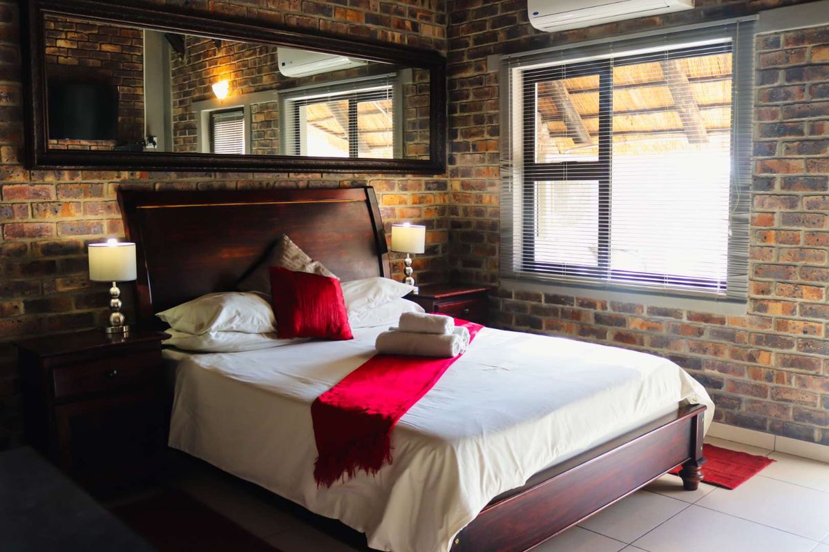 A well-maintained bedroom featuring rustic exposed brick walls, tiled flooring, and an integrated air conditioning unit for climate control.