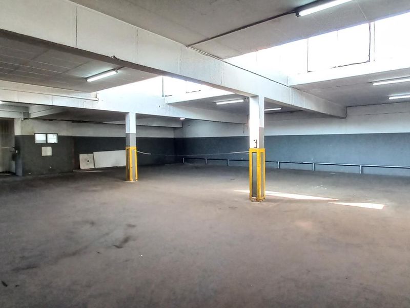 Spacious industrial warehouse or storage area featuring high ceilings, fluorescent lighting, concrete flooring, and structural support columns.