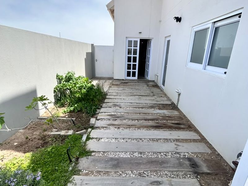A side exterior pathway featuring timber sleepers and pebble detailing, leading to a rear entrance with white-framed french doors and a solid boundary wall.
