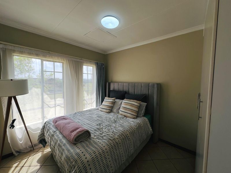 A well-lit bedroom featuring tiled flooring, built-in cupboard storage, and large grid-pane windows allowing for natural light.