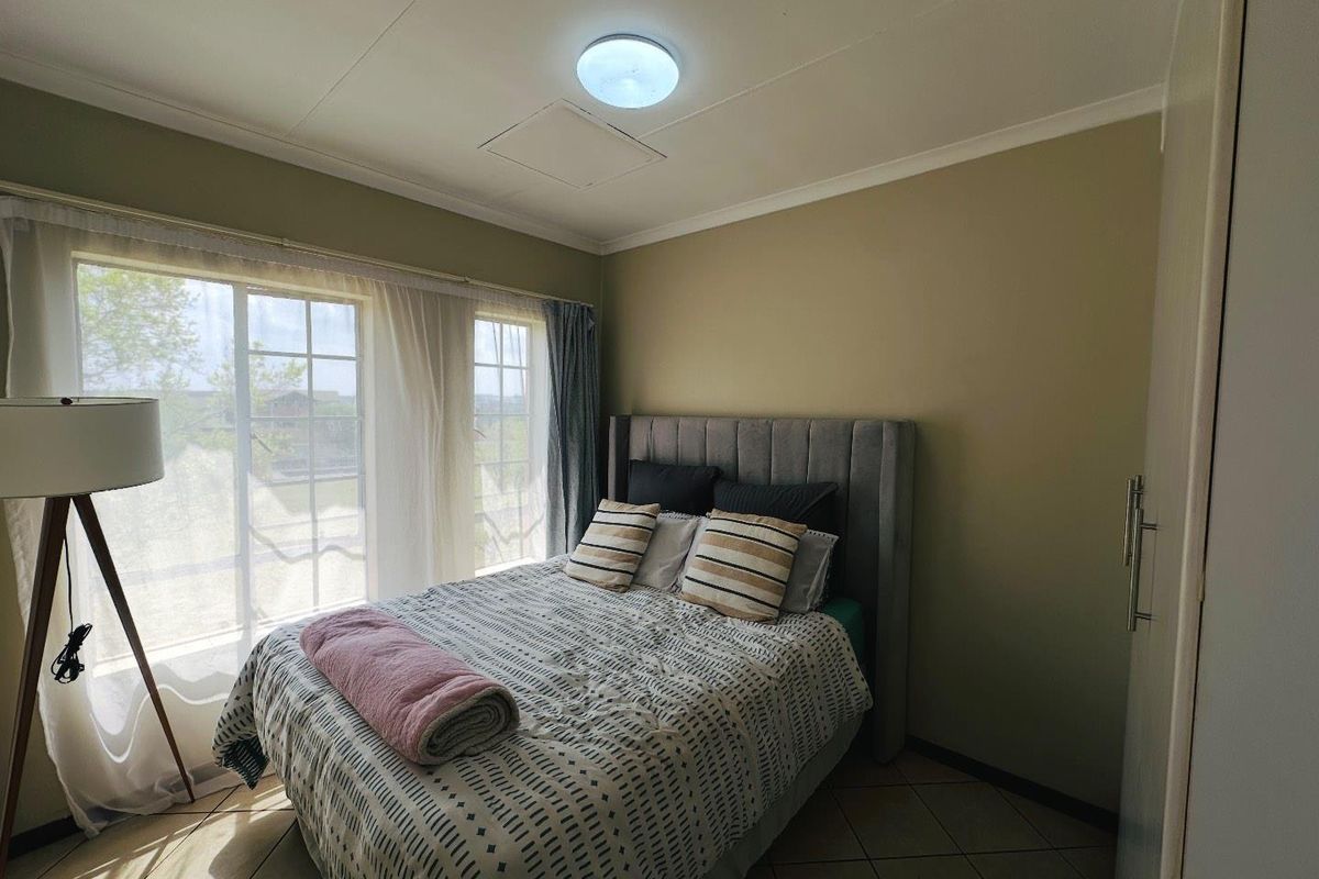 A well-lit bedroom featuring tiled flooring, built-in cupboard storage, and large grid-pane windows allowing for natural light.