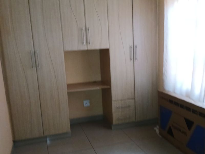 A bedroom featuring built-in wooden cupboards with an integrated desk area, tiled flooring, and a patterned ceiling.