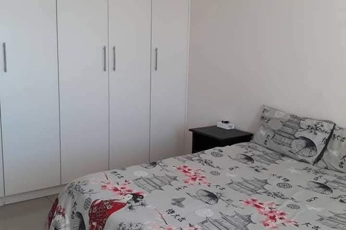 A clean bedroom featuring neutral tiled flooring and ample storage space provided by floor-to-ceiling built-in cupboards.