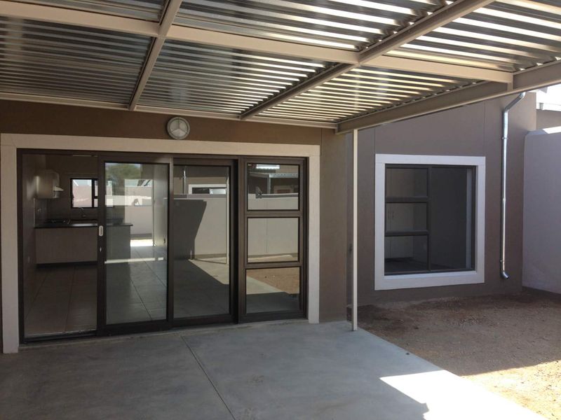A covered patio area featuring a corrugated metal roof, concrete flooring, and sliding glass doors providing access to the interior living space.