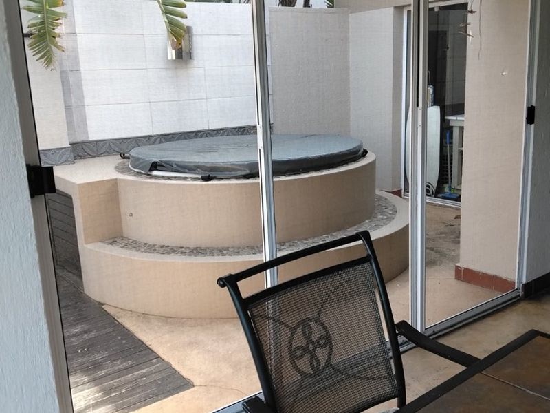 A covered patio area featuring a built-in circular jacuzzi, accessible through large sliding glass doors, providing a private outdoor relaxation space.