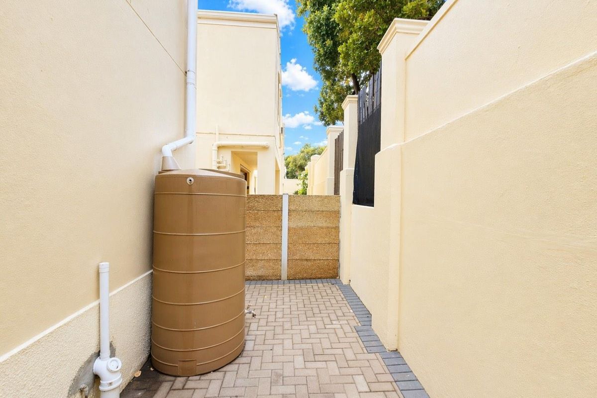 A side passage of the townhouse featuring paved flooring, a boundary wall, and a functional water tank installation.