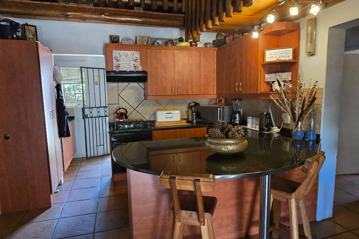 A functional kitchen featuring wooden cabinetry, granite countertops, a breakfast nook, and exposed timber ceiling beams, offering a warm and traditional aesthetic.