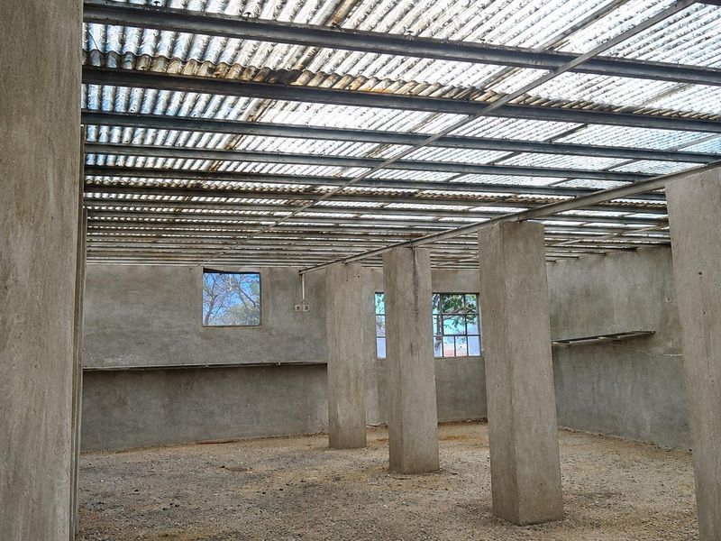 An unfinished utility space featuring concrete columns, exposed steel roof structure with translucent sheeting, and cement plastered walls, offering a blank canvas for development.