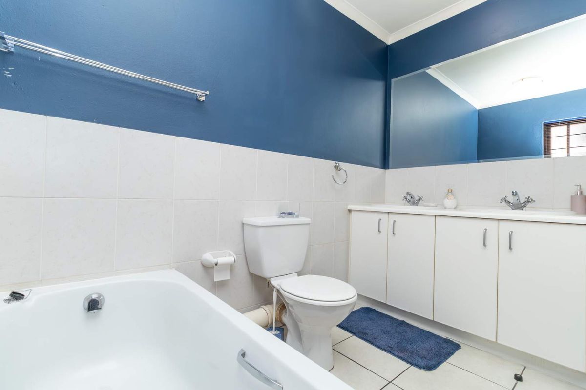 A functional bathroom featuring a white bathtub, a dual-basin vanity with white cabinetry, and a toilet, finished with tiled flooring and blue accent walls.