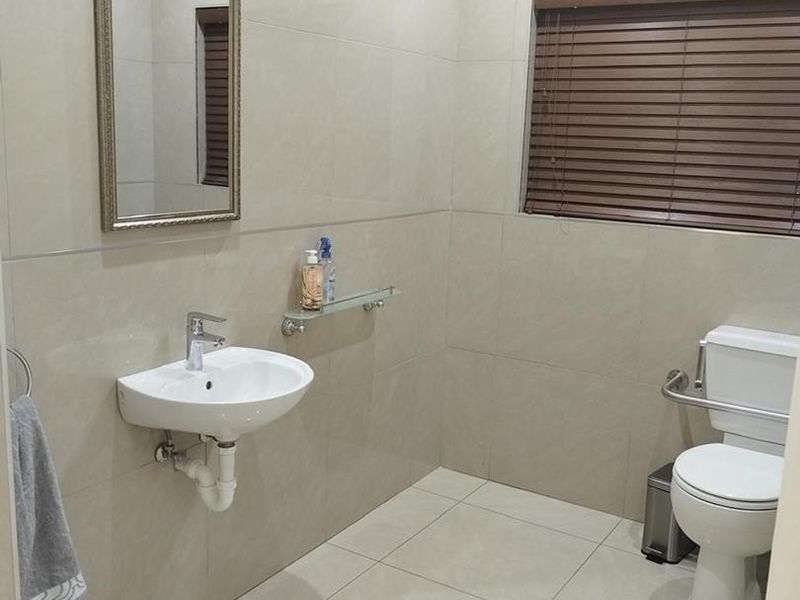 A clean, modern bathroom featuring neutral wall and floor tiles, a wall-mounted basin, and a toilet with an integrated grab rail.