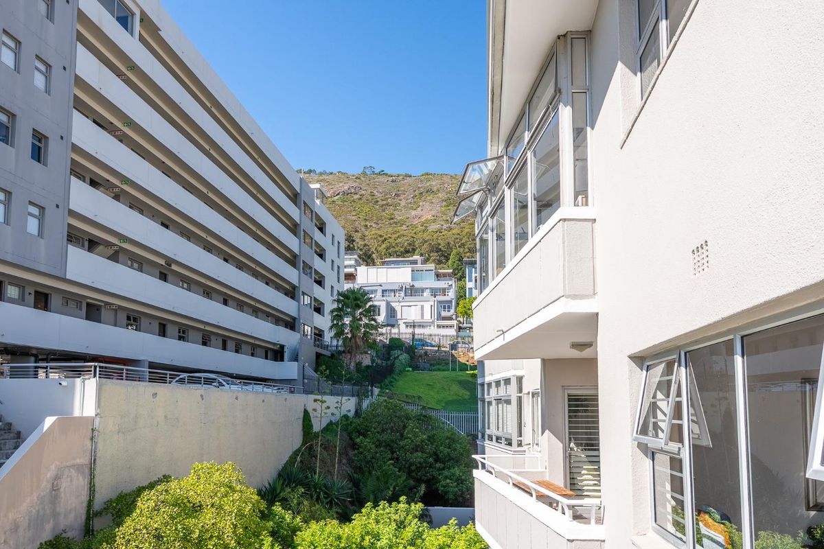 Exterior view of the apartment building featuring balconies, aluminium window frames, and a landscaped garden area with a mountain backdrop.
