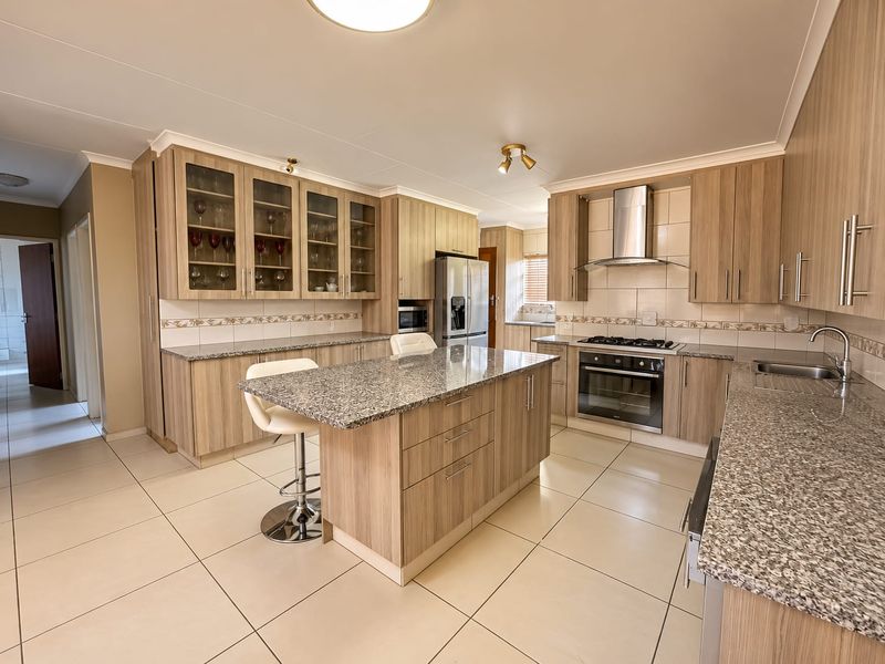Modern kitchen featuring light wood cabinetry, granite countertops, a central island, and integrated stainless steel appliances, complemented by neutral tiled flooring.