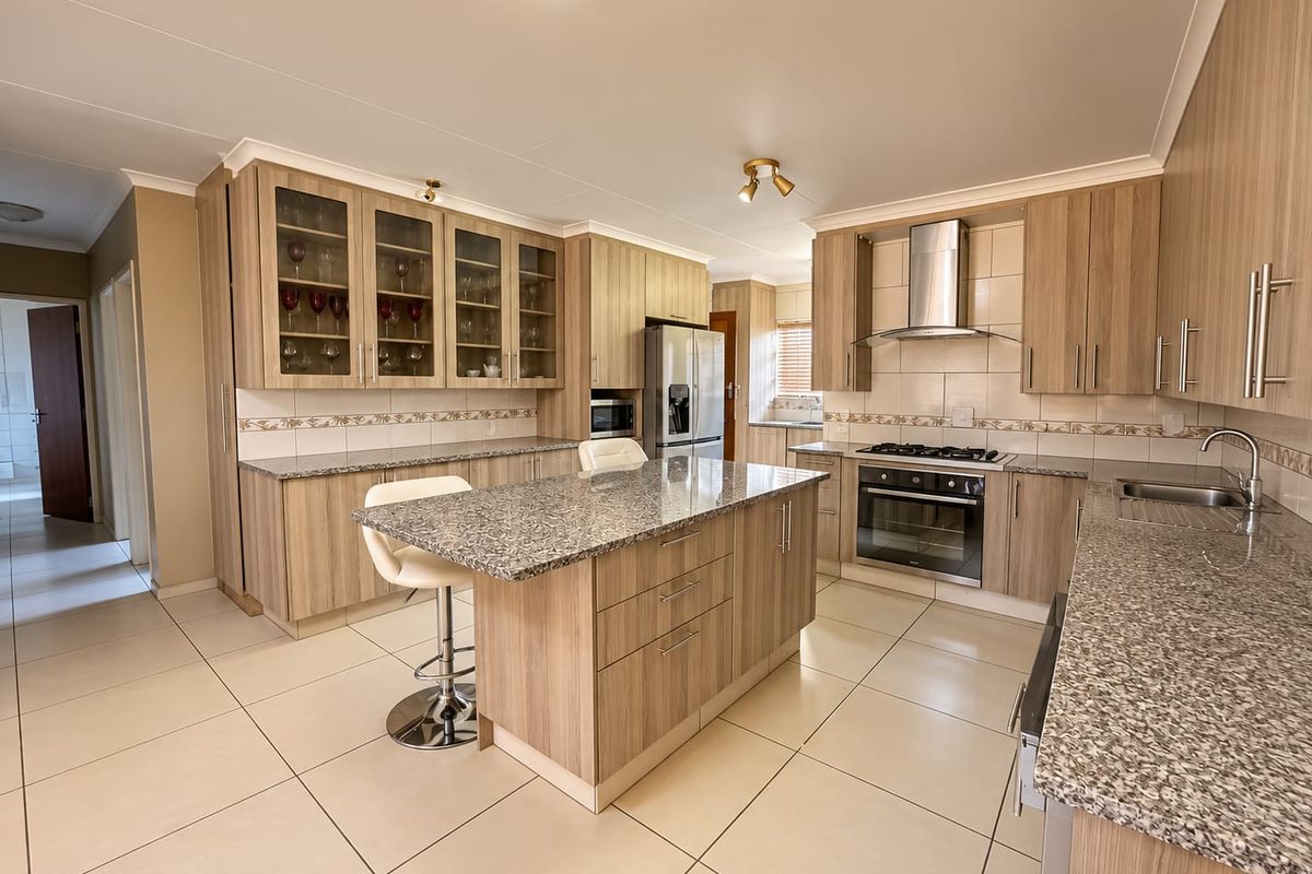 Modern kitchen featuring light wood cabinetry, granite countertops, a central island, and integrated stainless steel appliances, complemented by neutral tiled flooring.
