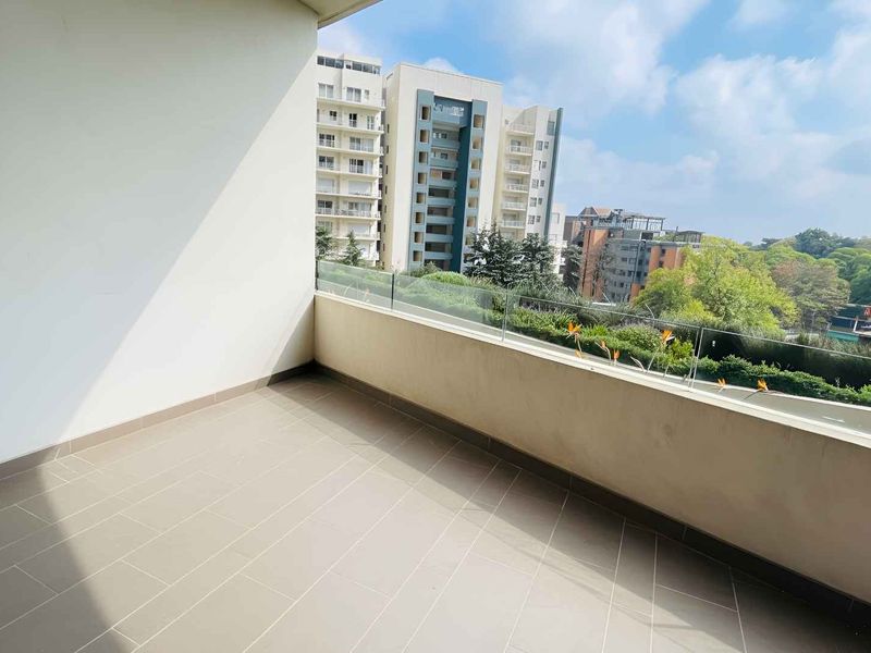 A clean, modern balcony featuring tiled flooring and a sleek glass balustrade, offering an open view of the surrounding urban landscape.