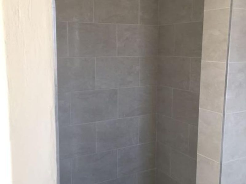 A clean, modern walk-in shower featuring neutral wall tiles and a contrasting mosaic floor tile finish.