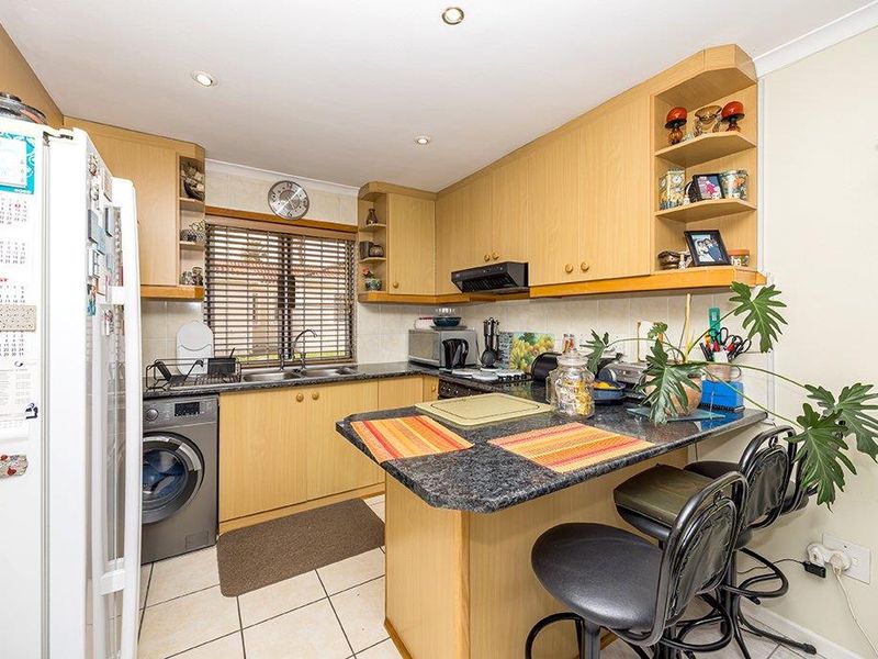 Functional kitchen featuring light wood-tone cabinetry, dark laminate countertops, a double bowl sink, and integrated laundry plumbing, offering a practical layout.
