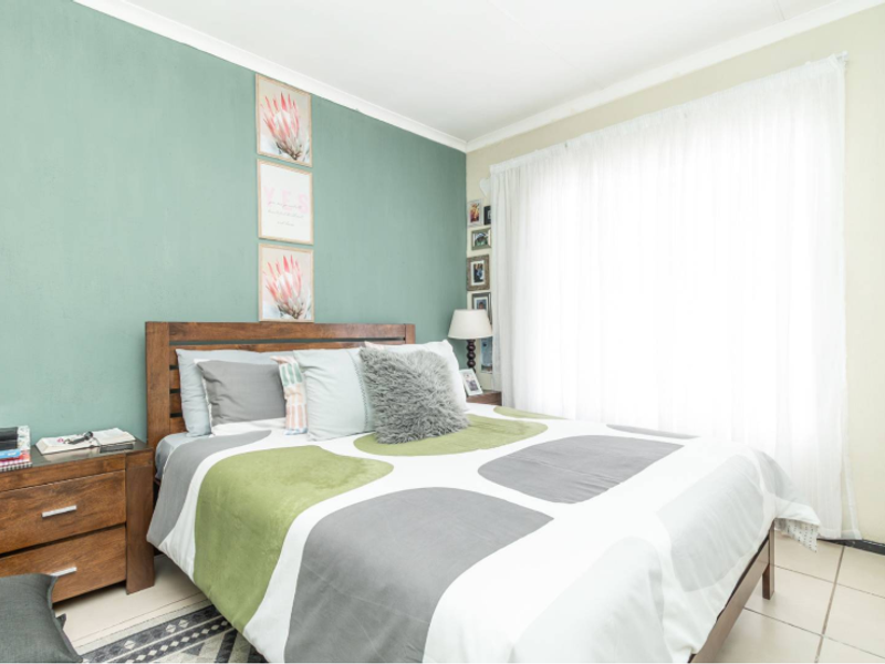 A bedroom featuring tiled flooring and a built-in cupboard, with a green accent wall and natural light from the window.