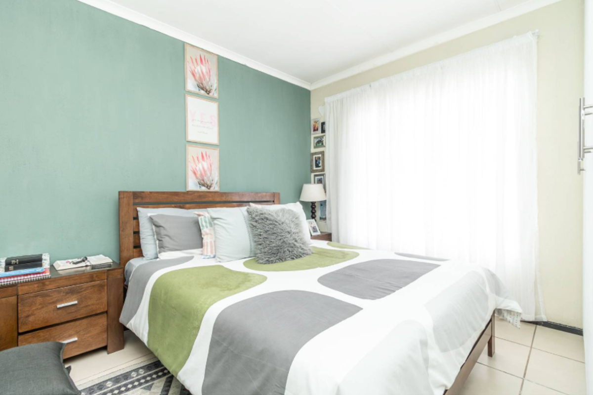 A bedroom featuring tiled flooring and a built-in cupboard, with a green accent wall and natural light from the window.